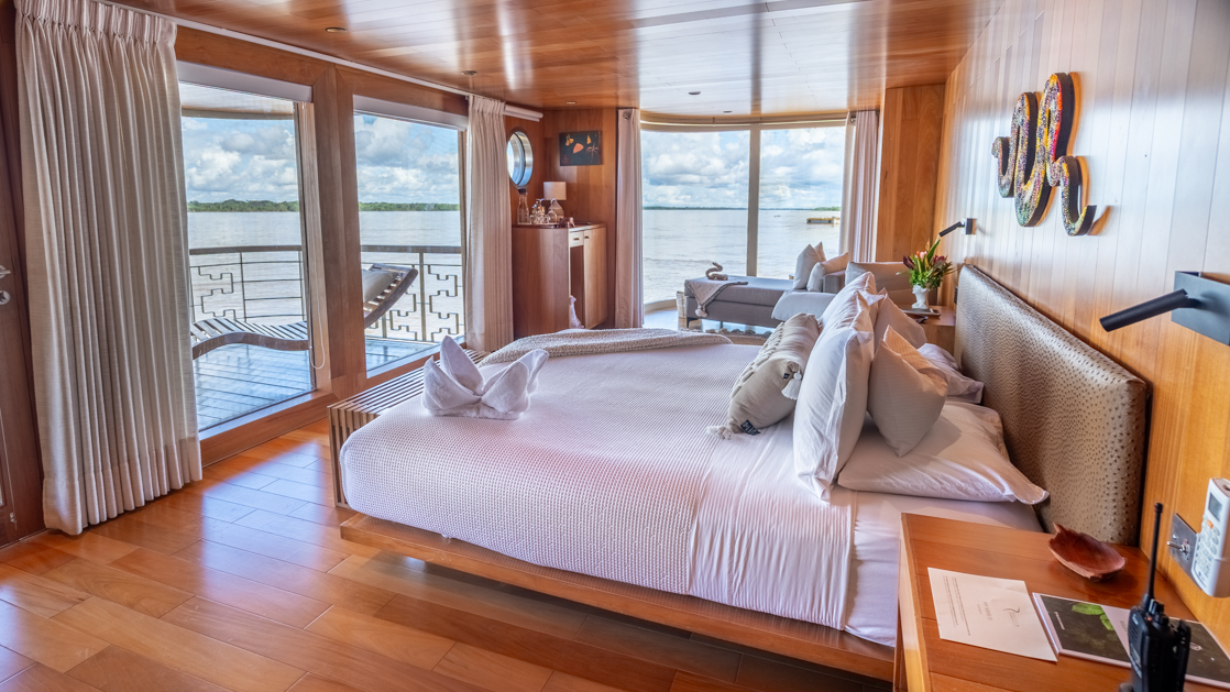 Master Suite bedroom aboard Delfin I with a double bed with white sheets, large floor-to-ceiling windows, and a small hot tub on the deck
