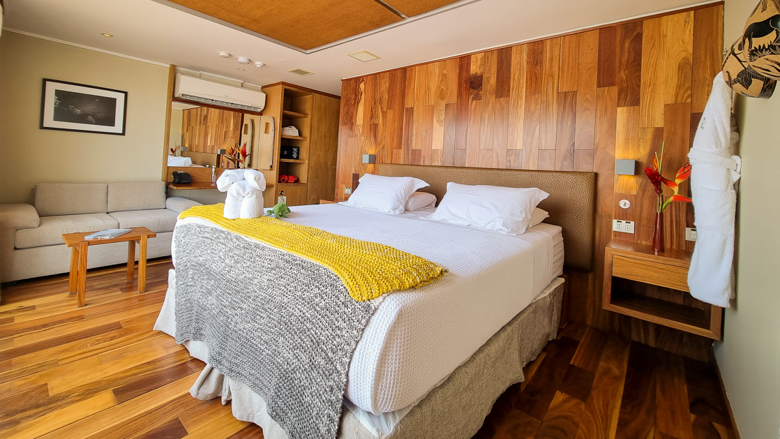 Upper Suite on Delfin III Amazon riverboat with wood finishes & large double bed in white linens.
