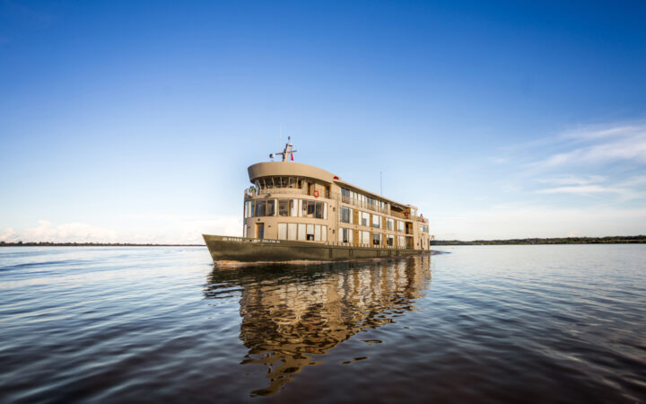 Exterior of bow and port side of Delfin III riverboat at rest in calm water under blue sky during an Amazon River cruise.