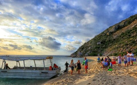 adventure travelers relax on a desolate beach at sunset with a skiff anchored on shore during the great barrier reef australia cruise