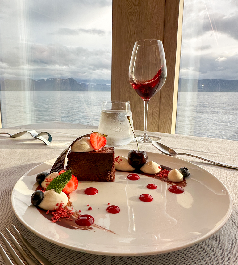 Delicious dessert with chocolate cake, berries, next to a red glass of wine on a table aboard national geographic endurance in Iceland
