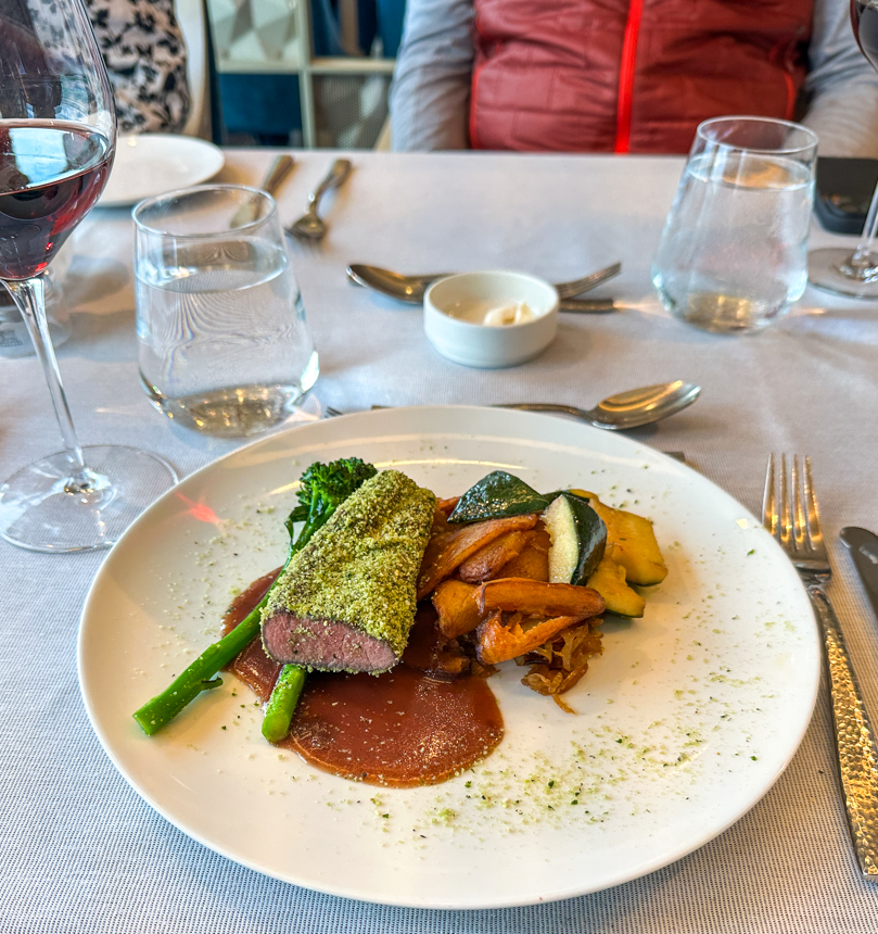 Lamb dinner with cooked vegetables and a red sauce on a bright on a white table, next to water glasses on the national geographic endurance