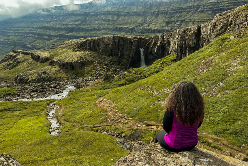 Women sitting on a rock looking out at a nearby waterfall, lush green landscapes and on a misty cloudy day in Iceland