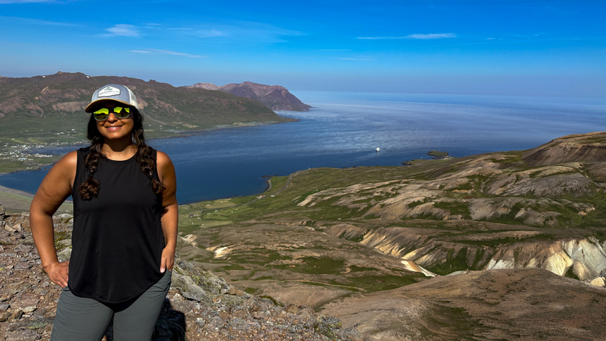 Women with hat and sunglasses on standing at the top of lookout point looking down at a large bay of water in Iceland