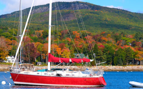 Red sailboat anchored in the bay of the east coast off the coast in front of green and brown trees
