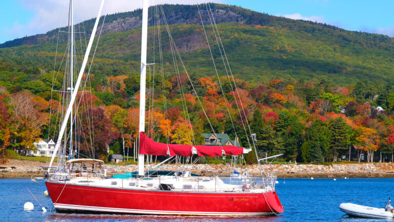 Red sailboat anchored in the bay of the east coast off the coast in front of green and brown trees