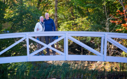 Couple standing on small white bridge in front of green small creek