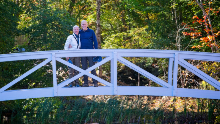 Couple standing on small white bridge in front of green small creek