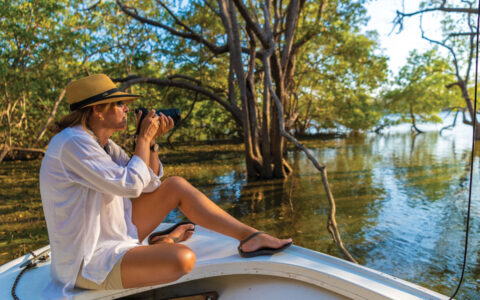Women in white shirt and tan hat photographing off a small boat