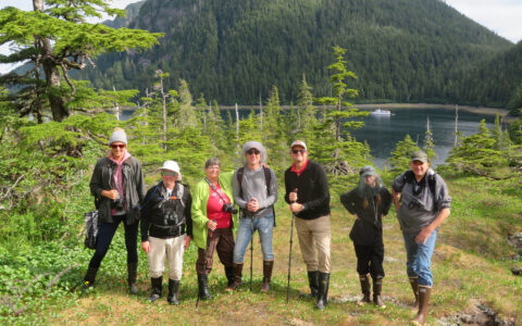 Family yacht charter guests pose above a forested cove in Prince William Sound.