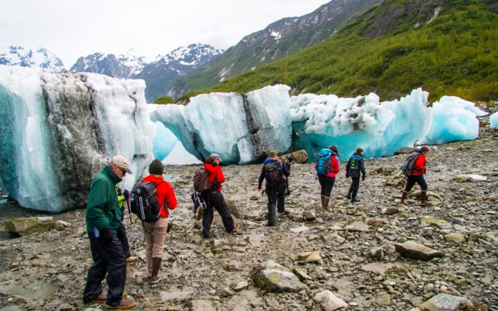 As part of a shore excursion, a group of travelers walks past large teal beached icebergs that washed ashore in Alaska.
