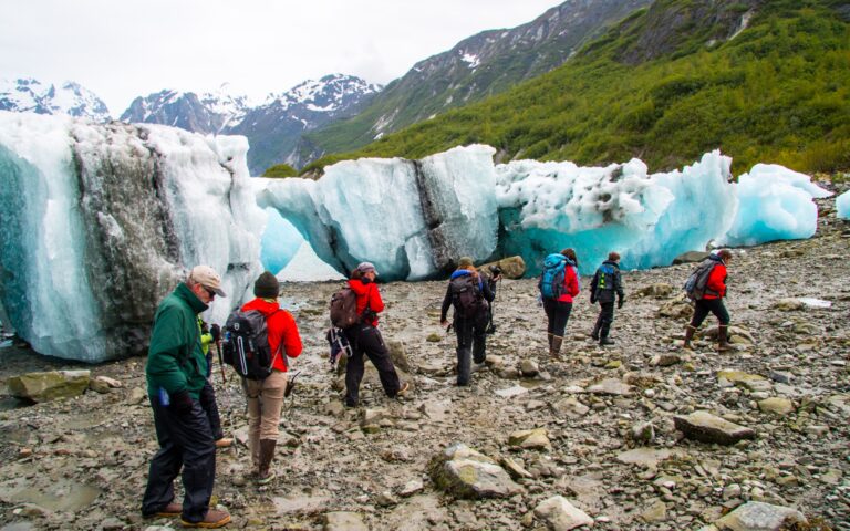 As part of a shore excursion, a group of travelers walks past large teal beached icebergs that washed ashore in Alaska.