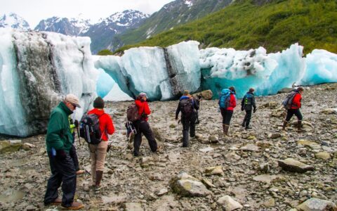 As part of a shore excursion, a group of travelers walks past large teal beached icebergs that washed ashore in Alaska.