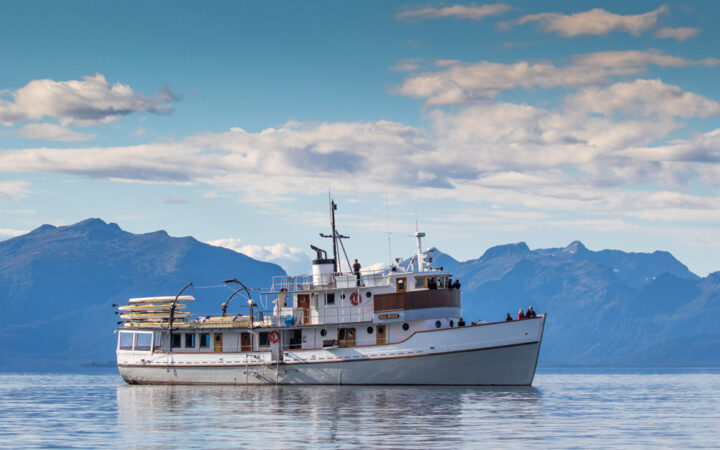 Exterior of Sea Wolf ship with white wood decks & trim, stacked yellow kayaks & classic yacht look.