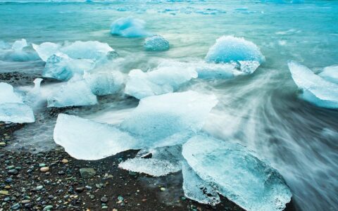 Sheets of crystal teal ice wash ashore to a black sand beach in Iceland seen aboard Wild Iceland Escape Arctic cruise.