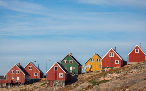 Seven brightly colored red, green and yellow houses seen on a rocky hill in Ittoqqortoormiit Greenland.