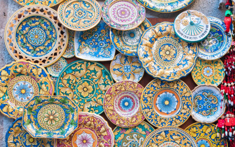 A colorful display of traditional Sicilian ceramic plates and bowls, featuring various patterns and designs, likely for sale in a shop or market.