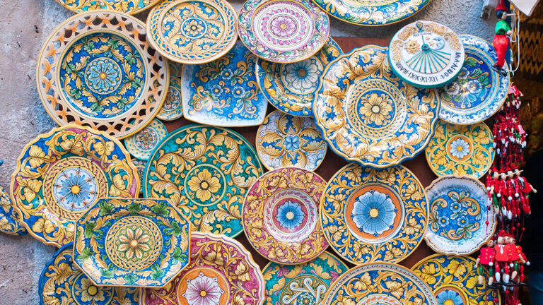 A colorful display of traditional Sicilian ceramic plates and bowls, featuring various patterns and designs, likely for sale in a shop or market.