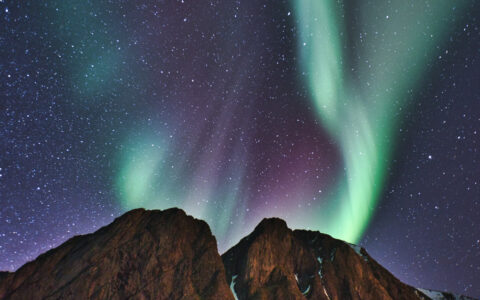 Green and purple streaks of Northern Lights seen above a rocky mountain at night, seen on a Northern Lights Explorer cruise.