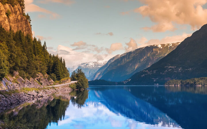 Hardangerfjorden seen on a Norway fjords cruise at sunset with pink clouds and blue still water