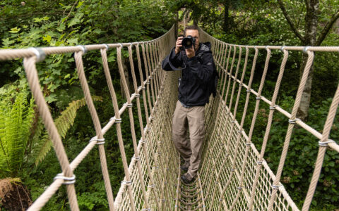 Photographer takes photo on rope bridge in lush gardens of Cornwall, England during the Ancient Isles Nat Geo cruise.