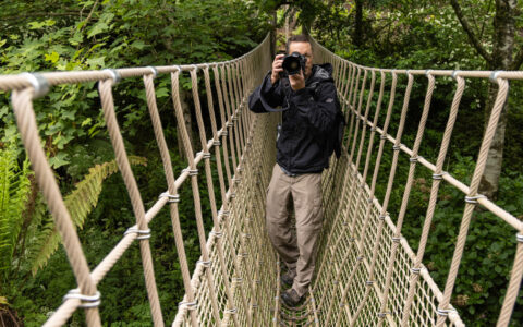 Photographer takes photo on rope bridge in lush gardens of Cornwall, England during the Ancient Isles Nat Geo cruise.
