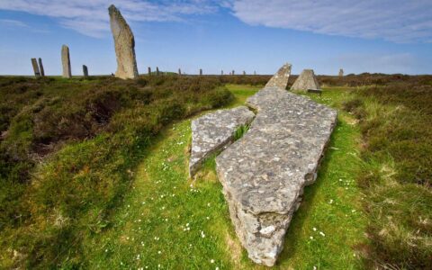 Ring of Brodgar ancient stone circle sits in green grass under blue skies in Orkney Islands, Scotland.