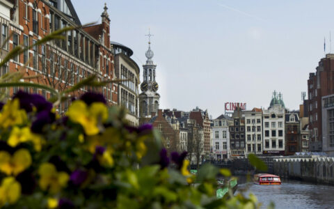 Amnsterdam cannaels on a moody cloudy day with historic builings off in the distance and a small river boat cruising along the river.