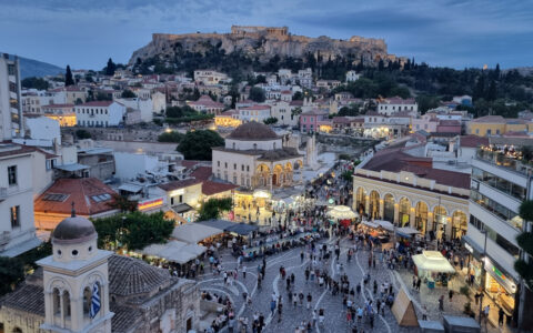Aerial view of busy square in Athens, Greece at dusk, with the Acropolis towering over everyone on a hillside.