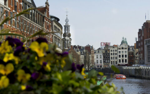 Amnsterdam cannaels on a moody cloudy day with historic builings off in the distance and a small river boat cruising along the river.
