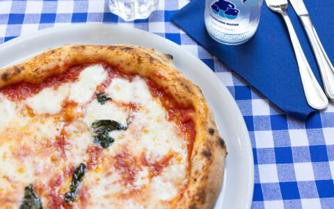 Freshly cooked Neapolitan-style margherita personal pizza on a blue-&-white checkered tablecloth in Naples, Italy.
