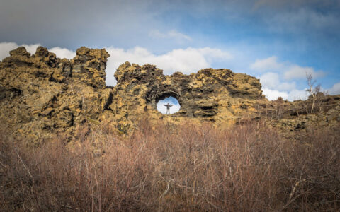 A traveler stands in a perfect circle cave in the rocks at Dimmuborgir Iceland
