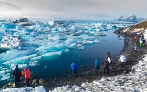 Jokulsarlon glacier lagoon in Iceland seen with travelers walking along the shoreline with the water filled with icebergs