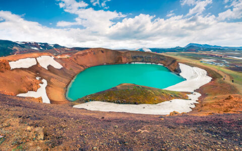 The vibrant blue Myvatn Lake seen with patches of snow around it in Iceland