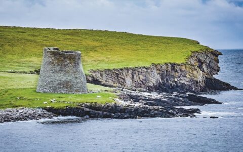 Mousa Broch seen among green grass waterfront on Mousa island in Shetland, Scotland, is the finest preserved example of an Iron Age broch or round tower.