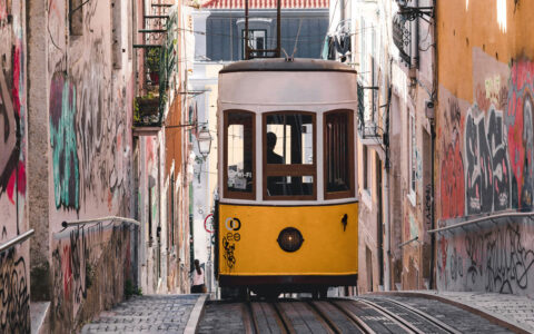 Yellow & white cable car climbs stone street between two graffitied buildings in Lisbon, Portugal, seen on the Med Feast cruise.
