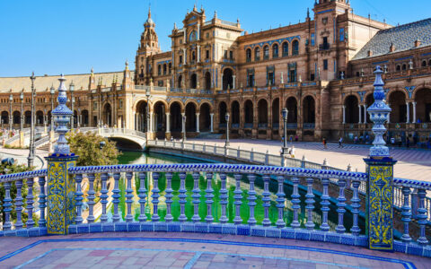 Blue-tile bridge over a turquoise moat surrounded by a circular beige brick building in Seville, Spain, seen on the Med Feast cruise.