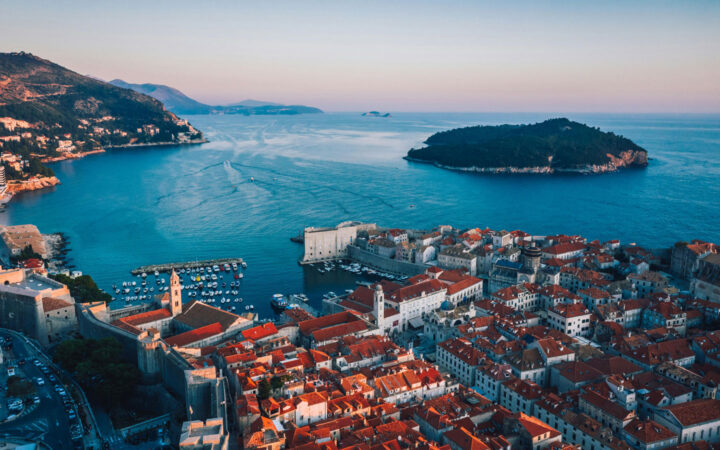 Aerial view of Dubrovnik, Croatia's seaside city with terracotta roofs, ancient walls & small harbor.