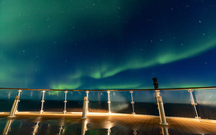 Green streaks across dark blue sky seen off the bow of a small ship on the Northern Lights Explorer cruise in the Arctic.
