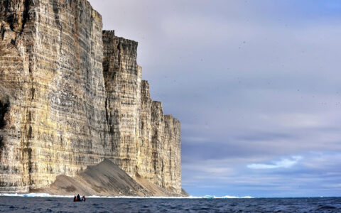 A giant cliff dwarfs a zodiac full of Northwest Passage expedition travelers at Prince Leopold Island