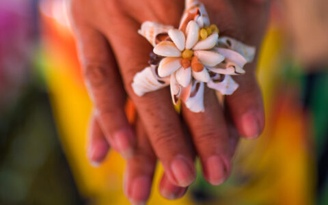 Close up of a woman's hands laid on top of each other to show off a shell ring forming a white flower.