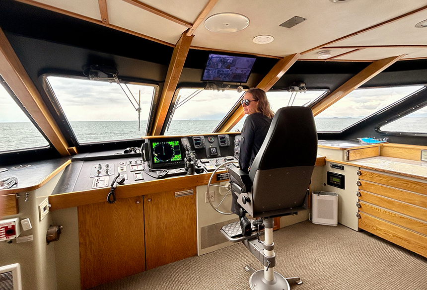 Safari Quest bridge, with captain sitting in chair at wheel with map, wide view windows, control consoles, navigation systems, and communication gear.