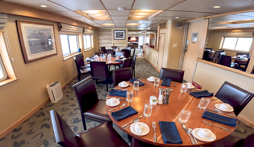 Dining room aboard Safari Quest. Three round tables set for dinner, with windows on one side and mirrors on the other.