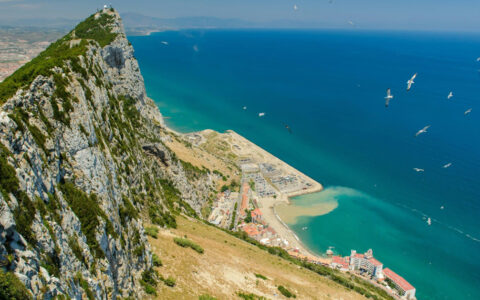 Overlook of Gibraltar rock looking down at the bright blue waters below with boats cruising around