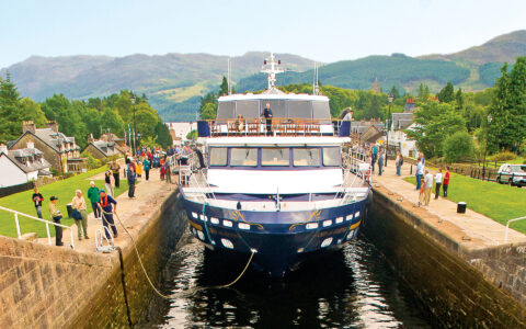 Small ship Lord of the Glens transiting the Caledonia Canal in Scotland with people watching