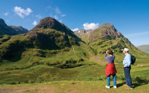 Man and woman admiring the view and taking a picture of the green mountains in Scotland