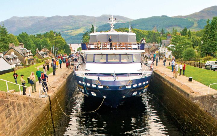 Small ship Lord of the Glens transiting the Caledonia Canal in Scotland with people watching