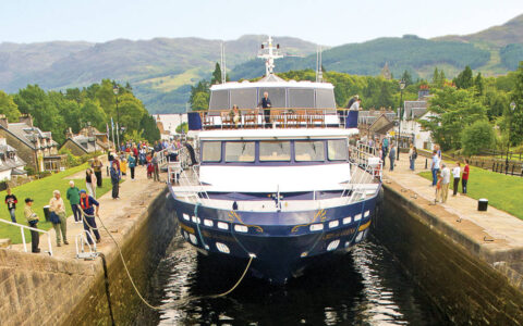 Small ship Lord of the Glens transiting the Caledonia Canal in Scotland with people watching