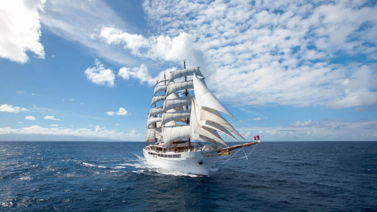 Sea Cloud II sailing off into the distance on a cloudy day with calm seas