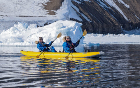 Two travelers kayak beside sea ice in Svalbard during an Arctic expedition cruise.